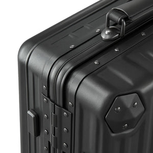 Close-up of a black hard-shell suitcase showing reinforced corners, rivet details, and a sturdy top carry handle.