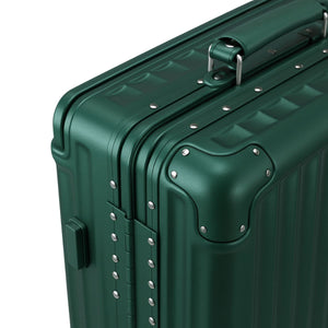 Close-up of a dark green hard-shell suitcase showing reinforced aluminum corners, rivet details, and a top carry handle.