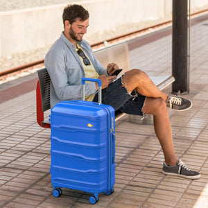 Man sitting on a bench with a blue suitcase at a train station.