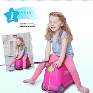 Little girl sitting on a pink BabyYuga ride-on suitcase, holding the pull strap and smiling, using it like a slide-on scooter.